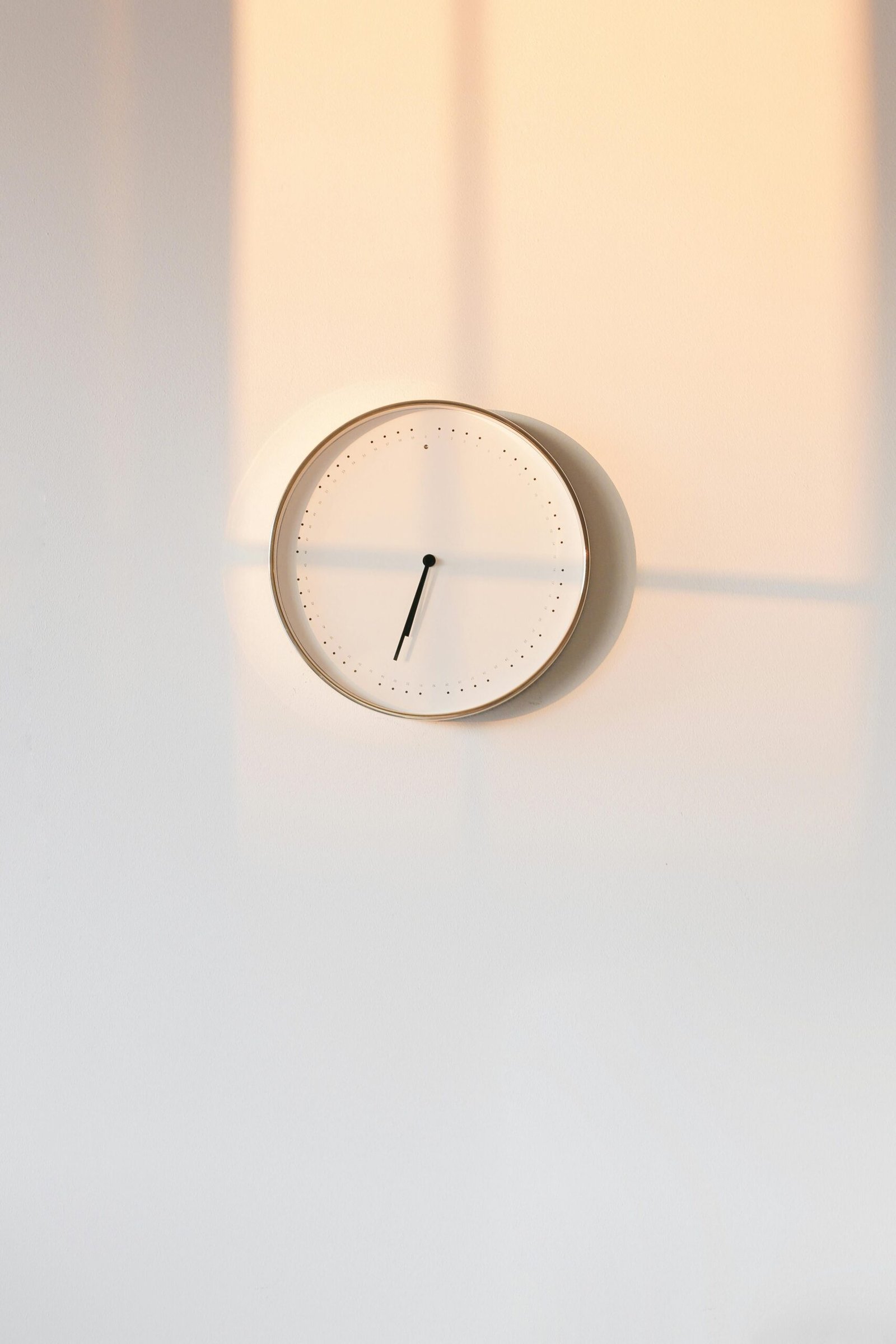 Elegant minimalist wall clock casting warm shadows on a simple backdrop.